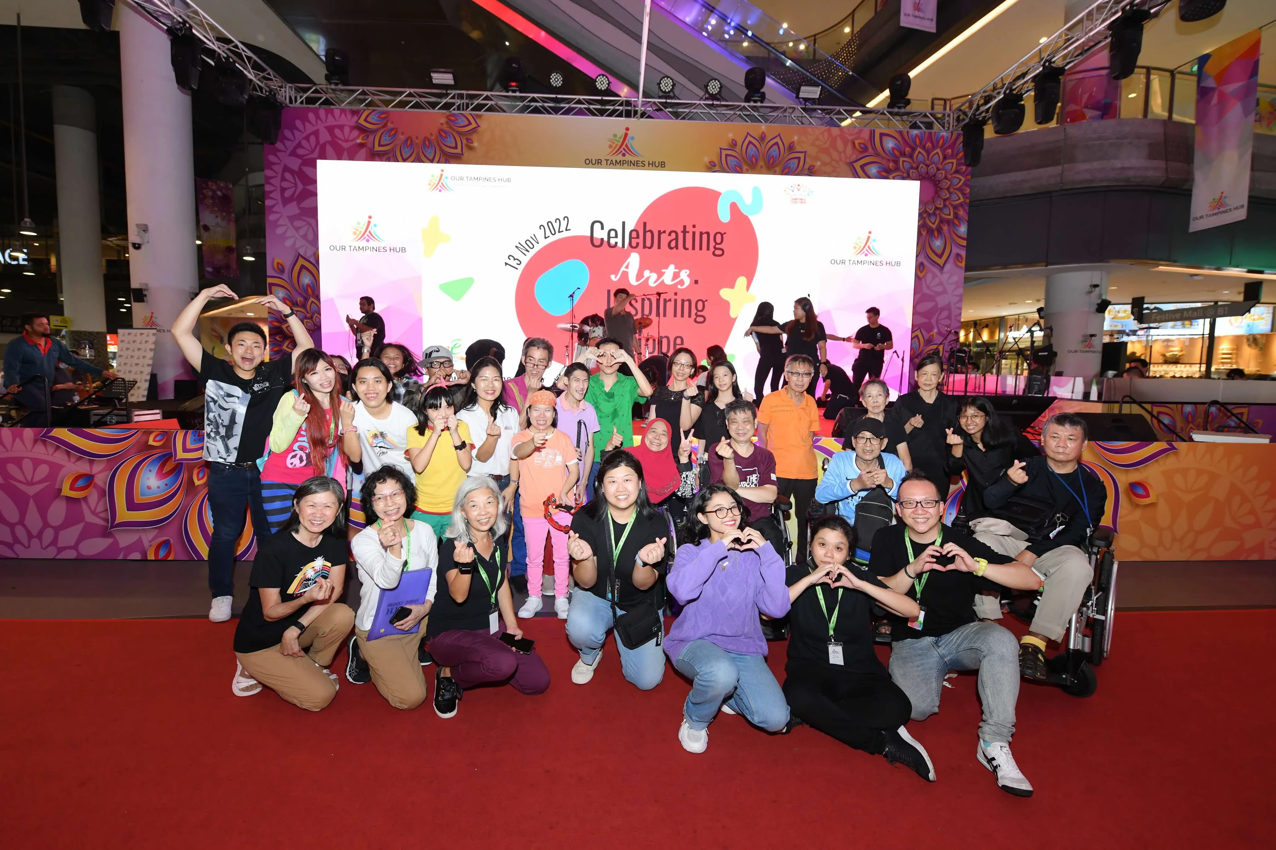 A group of people pose together in front of a stage with a "Celebrating Arts Inspiring Hope" banner.